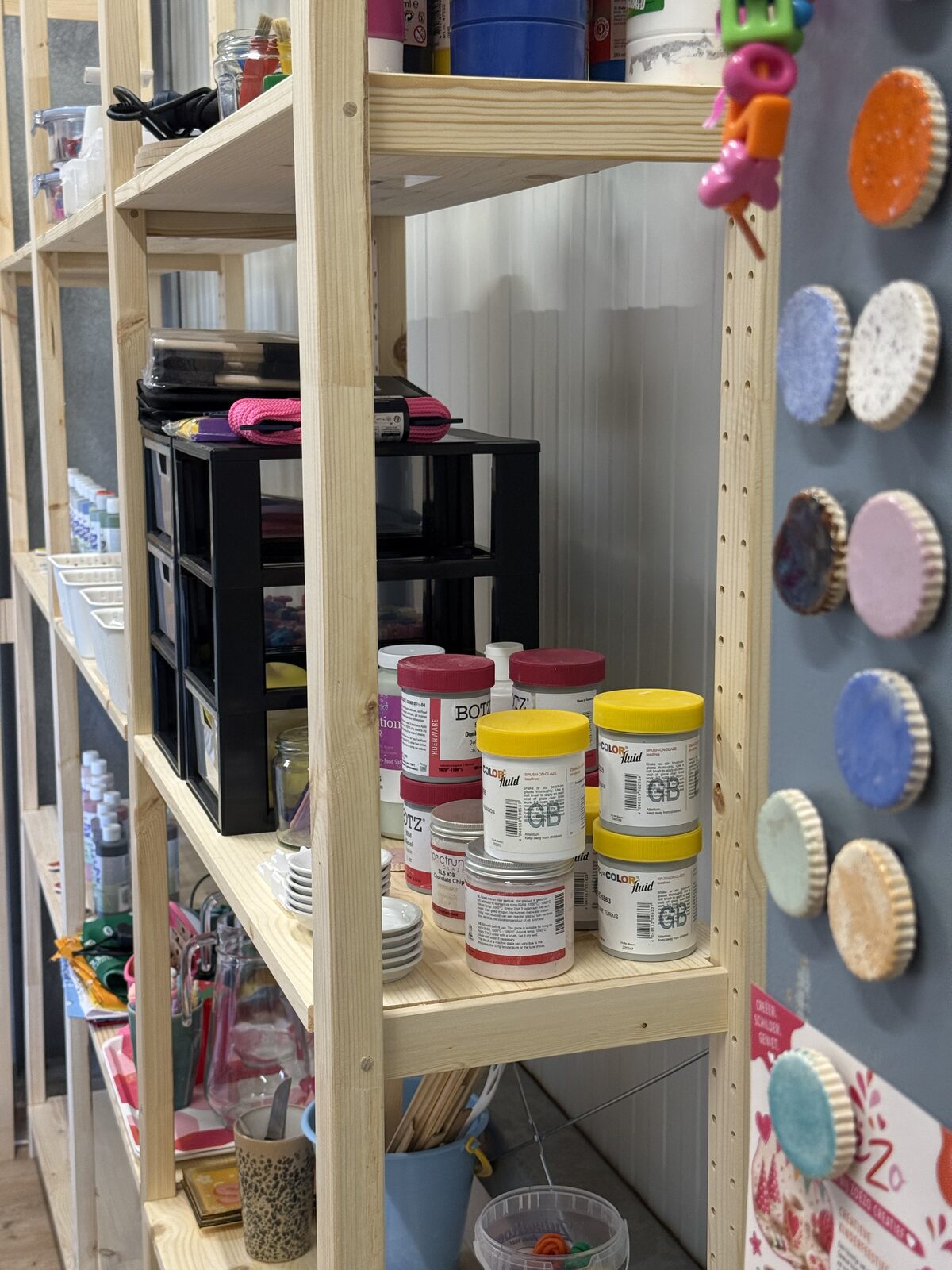Materialenkast met verf, kwasten en beschilderde voorbeeldbordjes aan de wand
